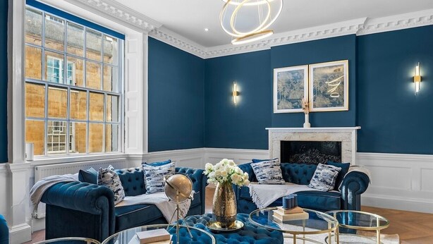 Ein Zimmer mit blauer Wand, Kamin, blauem Sofagarnitur und Glastisch.