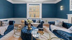 Ein Zimmer mit blauen Wänden, einem großen Fenster und einer blauen Sofagarnitur.