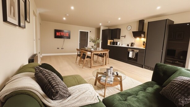 Ein modernes Wohnzimmer mit einem grünen Sofa, einem Couchtisch und einem Essbereich mit einem Holztisch und Stühlen.