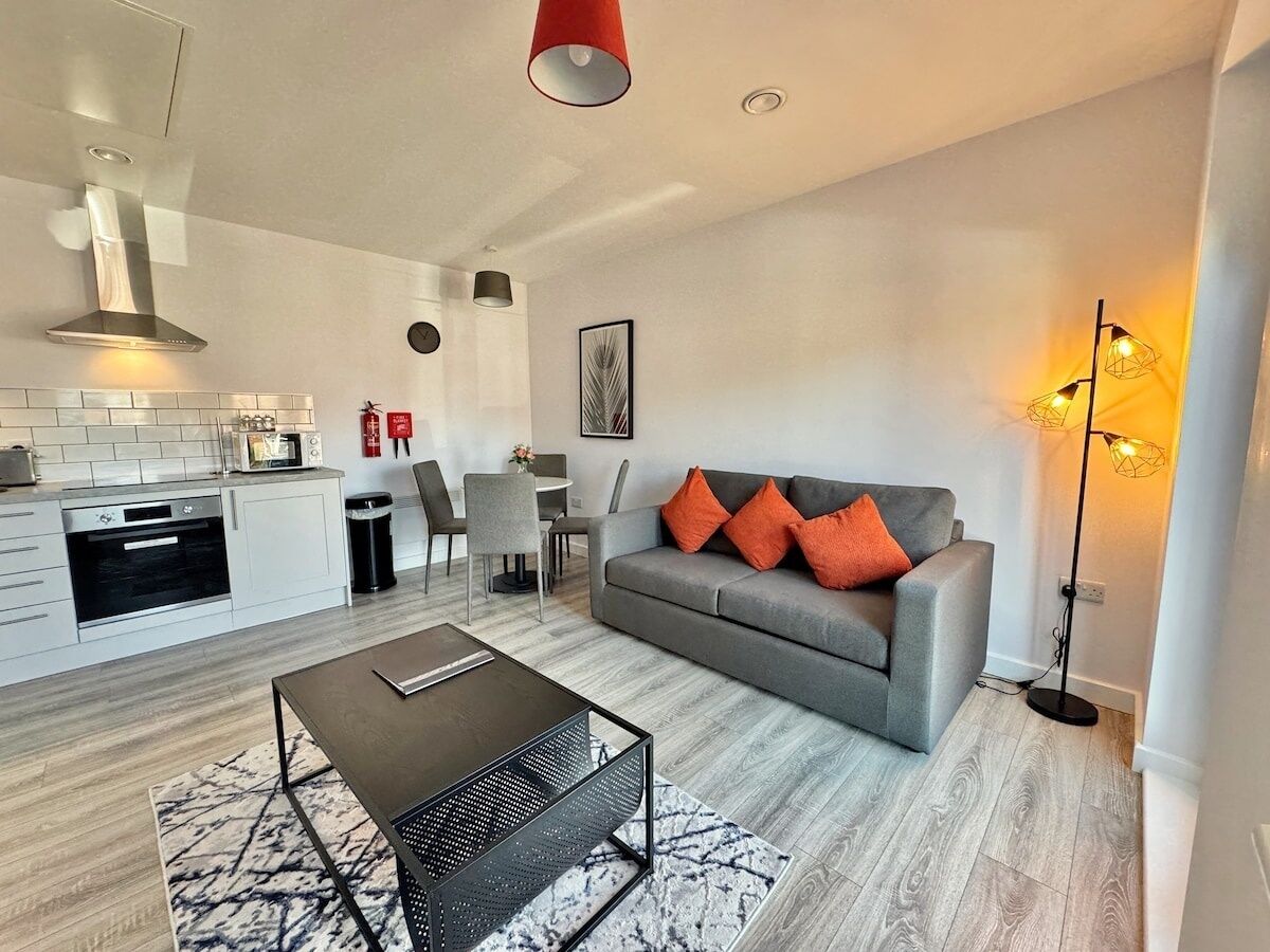 A modern living room with a grey sofa, a coffee table, and a dining area with a kitchen in the background.