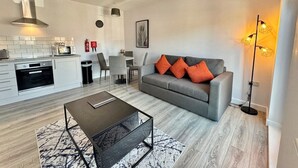 Ein modernes Wohnzimmer mit grauem Sofa, Couchtisch und Essbereich, im Hintergrund eine Küche.