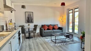 Eine moderne Küche mit grauen Schränken und einem Essbereich mit grauem Sofa und roten Kissen.