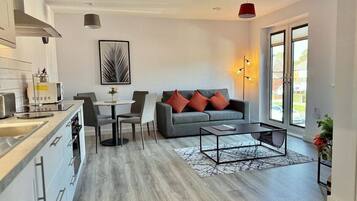 A modern kitchen with grey cabinets and a dining area with a grey sofa and red cushions.
