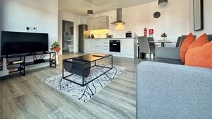 Ein modernes Wohnzimmer mit Fernseher, Couchtisch und grauem Sofa mit orangefarbenen Kissen.
