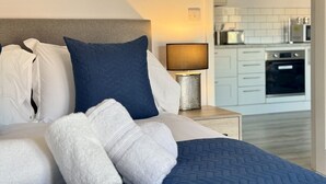 Ein Hotelzimmer mit Bett, Kissen, einer Nachttischlampe und Blick auf die Küche.