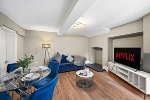 En moderne stue med spiseplads, sofa, sofabord og et fjernsyn, der viser Netflix-logoet.