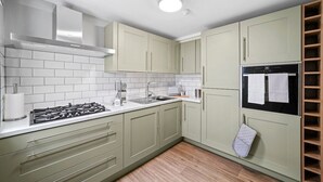 Een keuken met lichtgroene kastjes, witte metrotegels, een gasfornuis en een inbouwoven.