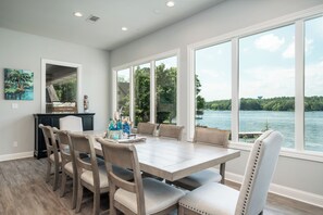 A dining area with a large table and chairs, a view of a lake, and a painting on the wall. - Oasis @ Bayshore - Lakefront Luxury 6BR w Stunning Views, Private Pool, Hot Tub (Hot Springs)