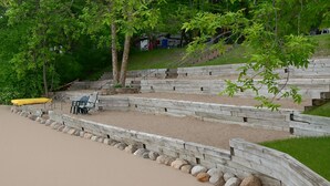 A sandy beach with wooden steps leading up to a seating area with chairs and a yellow kayak. - Lakefront retreat on West Battle Lake cozy, modern, and steps from the water! (Battle Lake)