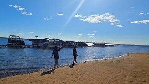 A beach with a clear sky, a few clouds, and a boat docked on the water. - Lakefront retreat on West Battle Lake cozy, modern, and steps from the water! (Battle Lake)