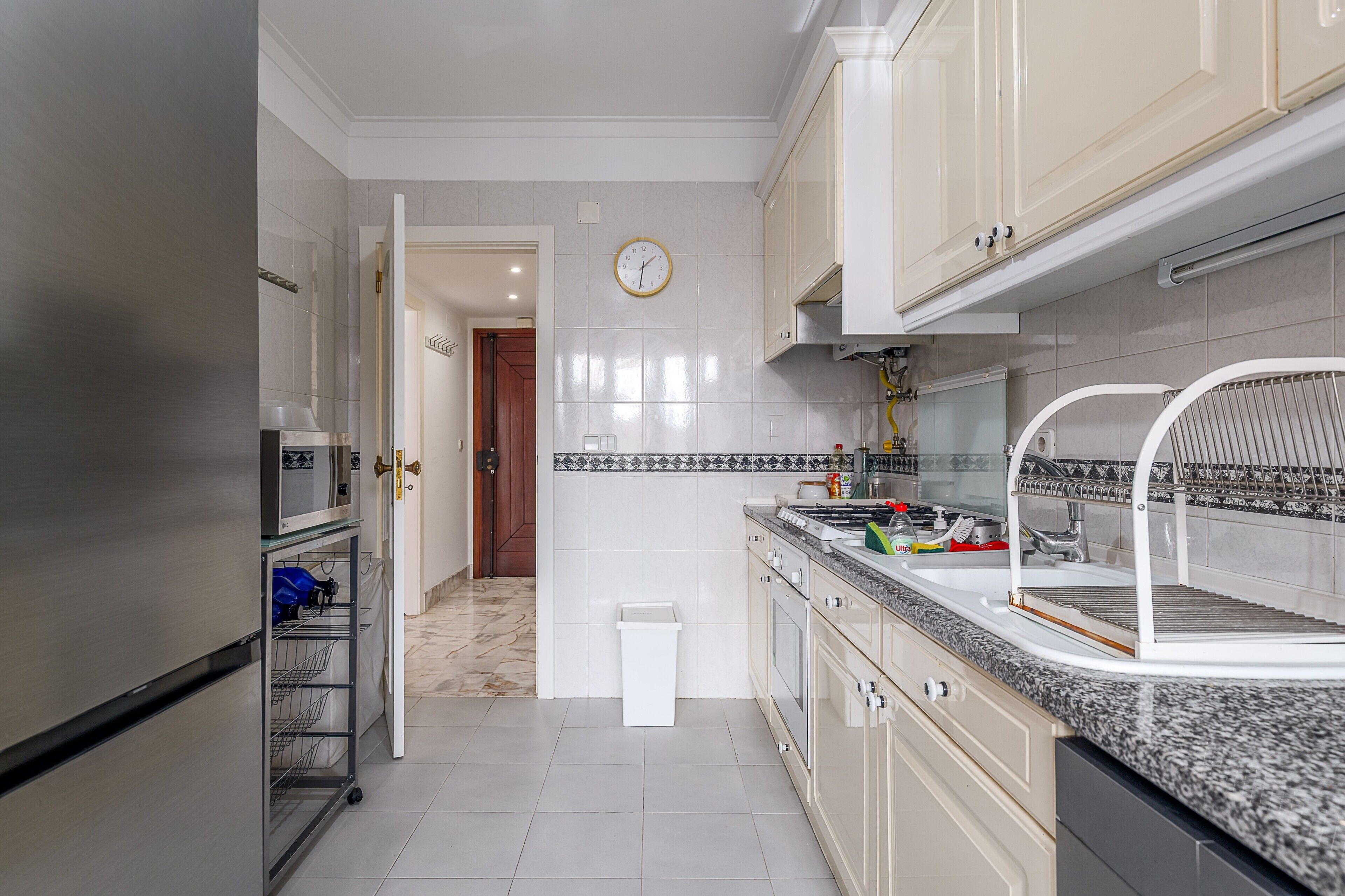 Una cocina moderna con electrodomésticos de acero inoxidable, un microondas, un lavabo con un tendedero y un reloj en la pared.
