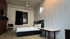 A bedroom with a bed, a chair, a table, and a TV on the wall.