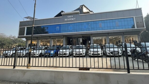 A modern building with a sign reading "SARA RESIDENCY." It features a large glass facade and a parking lot with several cars.