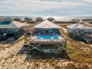 A beachfront property with multiple houses connected by walkways, a central pool area, and a view of the ocean. - Luxurious Coastal Home with Heated Pool and Views (Dauphin Island)