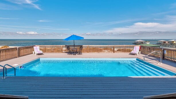 A swimming pool with a wooden deck, lounge chairs, and a view of the ocean. - Luxurious Coastal Home with Heated Pool and Views (Dauphin Island)