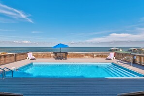 A swimming pool with a wooden deck, lounge chairs, and a view of the ocean. - Luxurious Coastal Home with Heated Pool and Views (Dauphin Island)