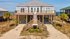 A beachfront house with a wooden deck and a staircase leading to a covered area. - Luxurious Coastal Home with Heated Pool and Views (Dauphin Island)