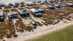 An aerial view of a coastal area with multiple beachfront properties, including houses and beach huts, connected by pathways and featuring direct access to the beach. - Luxurious Coastal Home with Heated Pool and Views (Dauphin Island)