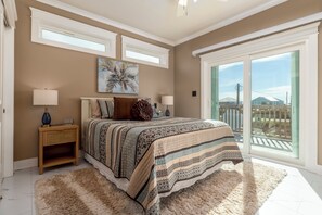 A bedroom with a large bed, two bedside tables, a window, and a view of the outside. - Luxurious Coastal Home with Heated Pool and Views (Dauphin Island)
