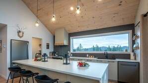 A modern kitchen with a large island, bar stools, a view of the outdoors, and a wooden ceiling.