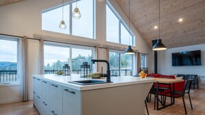 A modern kitchen with a large island, large windows, and a dining area with red cushions.