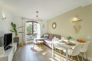 Ein modernes Wohnzimmer mit einer Couch, einem Esstisch, einem Fernseher und Topfpflanzen.