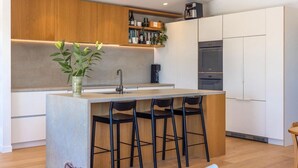 Eine moderne Küche mit Kochinsel, Barhocker, einer Kaffeemaschine und einem eingebauten Backofen.