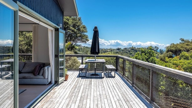 Eine Holzdachterrasse mit Glastür zum Balkon, ein Tisch mit Stühlen und ein schwarzer Sonnenschirm.