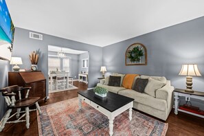 A living room with a sofa, coffee table, and a rug. There is a dining area with a table and chairs.