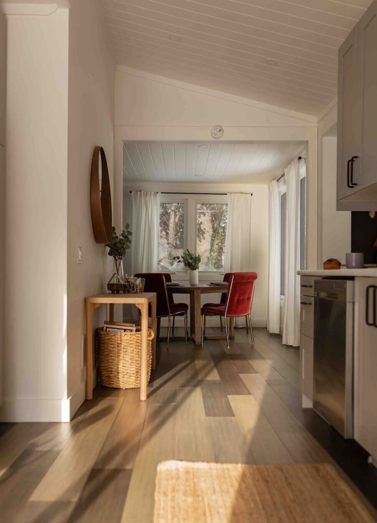 A modern kitchen with a dining area, wooden flooring, and a view of the outdoors.
