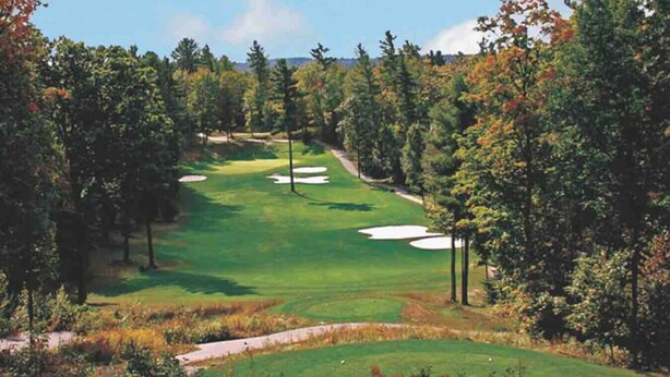 Ein Golfplatz mit Sandbunkern, einem Fußweg und dichter Baumvegetation.
