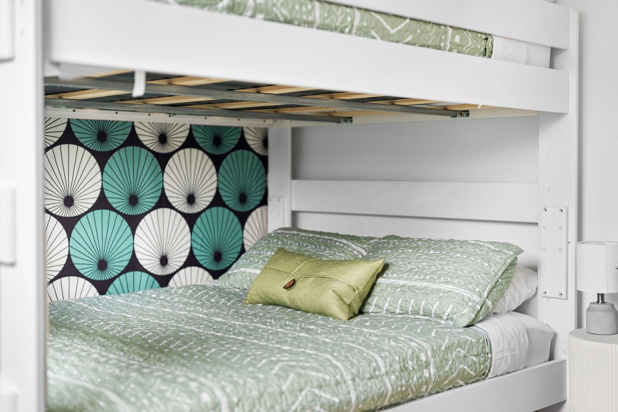 Una cama litera con un papel tapiz estampado y una mesita de noche con lámpara.