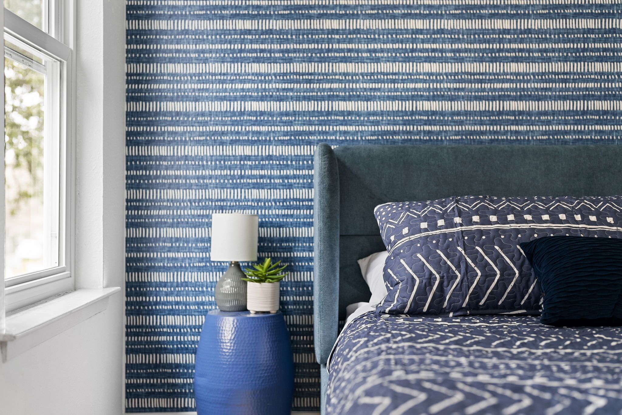 Une chambre à coucher avec un papier peint à motifs, une table de chevet avec une lampe et un lit avec une literie à motifs.