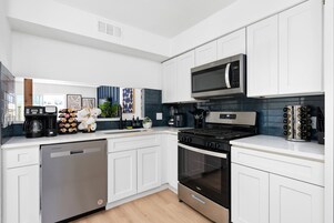 A modern kitchen with white cabinetry, a stainless steel dishwasher, a built-in oven, a microwave, and a coffee maker.