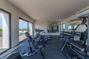 A modern gym with various exercise equipment, large windows, and a view of greenery outside. - Bucerias Ocean View 2 bdr new condo (Bucerías)