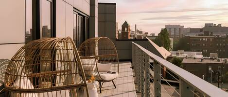 Un balcon avec des fauteuils en osier et une vue sur le paysage urbain.