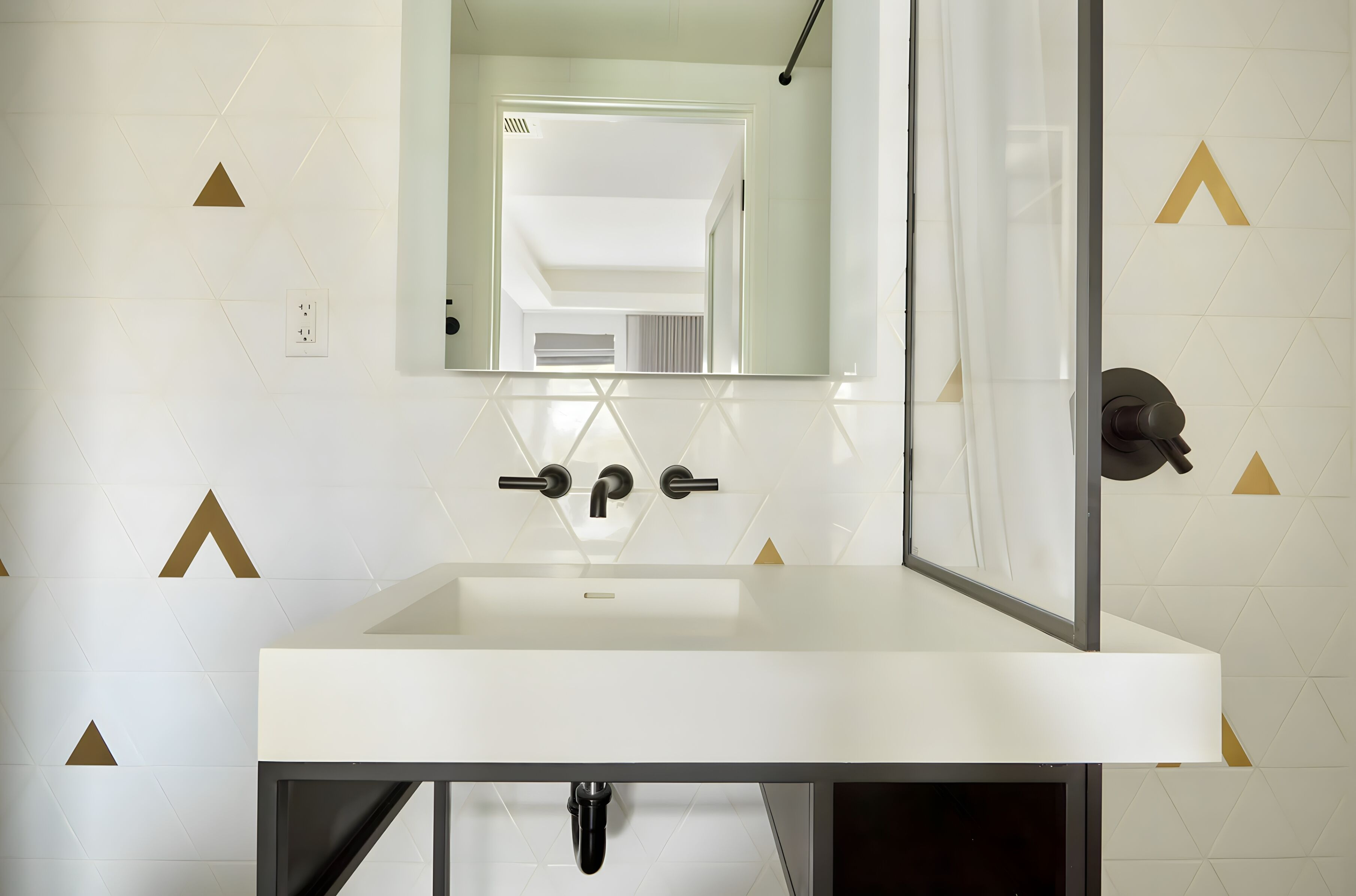 Un baño con lavamanos blanco, espejo y azulejos con diseño geométrico.