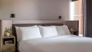 Una habitación de hotel con una cama grande, una mesita de noche con una planta y una ventana que da a un edificio de ladrillo.