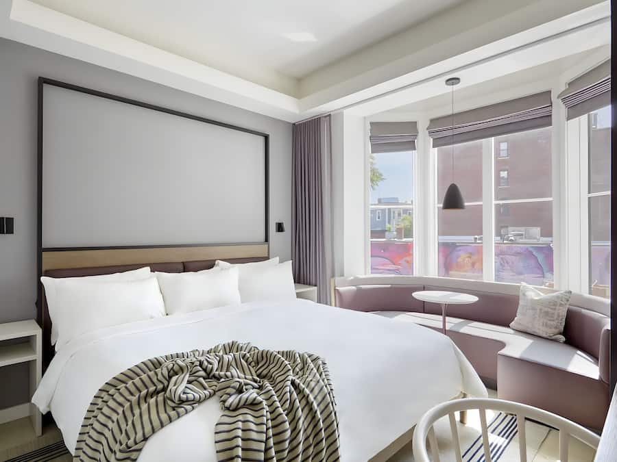 Habitación de hotel con una cama grande, un sofá, una mesita y una ventana con vistas a edificios.