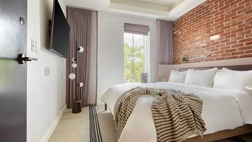 Habitación de hotel moderna con una cama grande, una pared de acento de ladrillo, un televisor de pantalla plana y vistas al exterior.