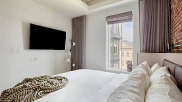 A hotel room with a large bed, a flat-screen TV mounted on the wall, a window with curtains, and a brick wall.