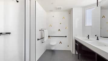 Ein modernes Badezimmer mit einem weißen Waschbecken, einem schwarzen Wasserhahn und einer weißen Toilette. Es gibt einen Duschbereich mit einer Glasduschtür und einem Handtuchhalter.