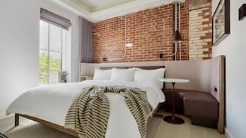 Une chambre d’hôtel moderne avec un grand lit, une petite table ronde, un banc et un mur en briques.