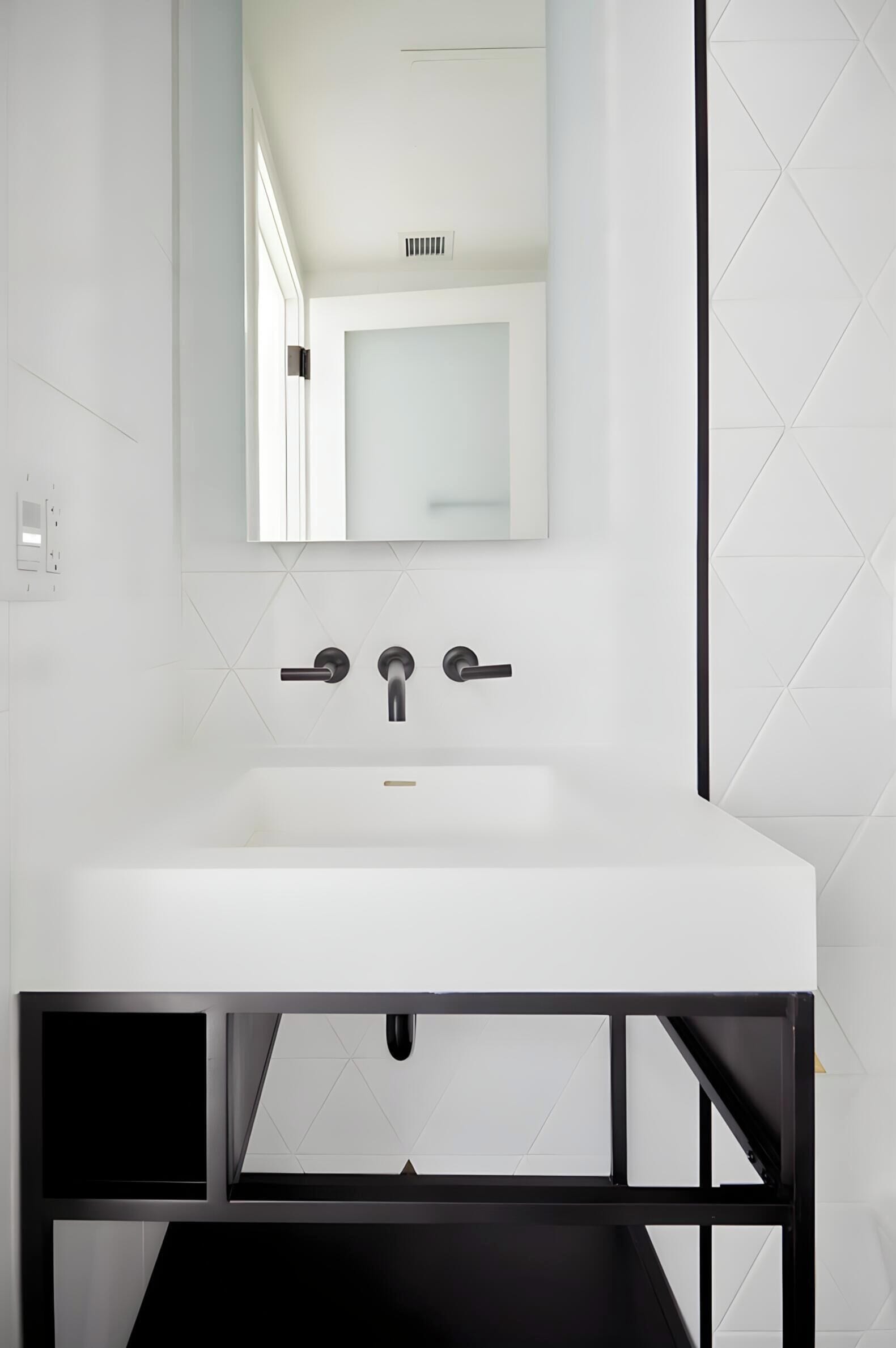 Une salle de bain moderne avec un lavabo blanc, un robinet noir et un miroir au-dessus.