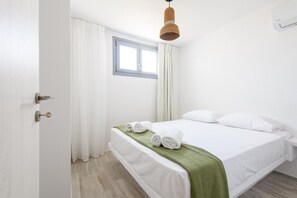 Ein Schlafzimmer mit einem Bett, weißen Vorhängen, einem Fenster und einer Pendelleuchte.