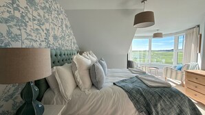 A bedroom with a large bed, a view of the outdoors, and a window with curtains. - A beautifully refurbished family home on Flexbury Park Road. (Cornwall)