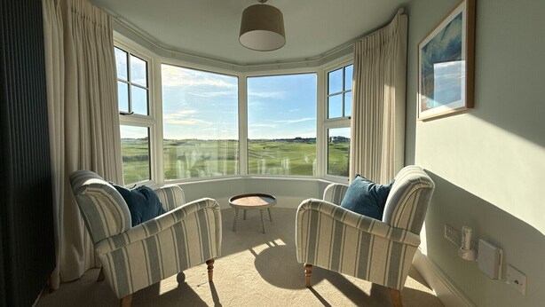 A room with two striped armchairs facing a round table, large windows with a view of a green landscape, and a ceiling light fixture. - A beautifully refurbished family home on Flexbury Park Road. (Cornwall)