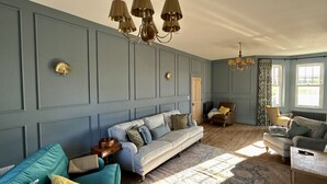A living room with a blue wall, a sofa, a chair, a coffee table, and a chandelier. - A beautifully refurbished family home on Flexbury Park Road. (Cornwall)