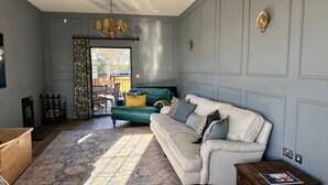 A living room with a green sofa, a white sofa, and a patterned rug. There is a chandelier hanging from the ceiling. - A beautifully refurbished family home on Flexbury Park Road. (Cornwall)