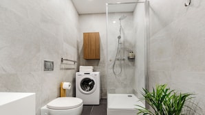 Une salle de bain moderne équipée de toilettes, d’un lave-linge, d’une douche et d’une plante.